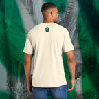 Man wearing an ivory t-shirt with a green Eternal Optimist Golf Club logo on the back, standing against an abstract-patterned wall.