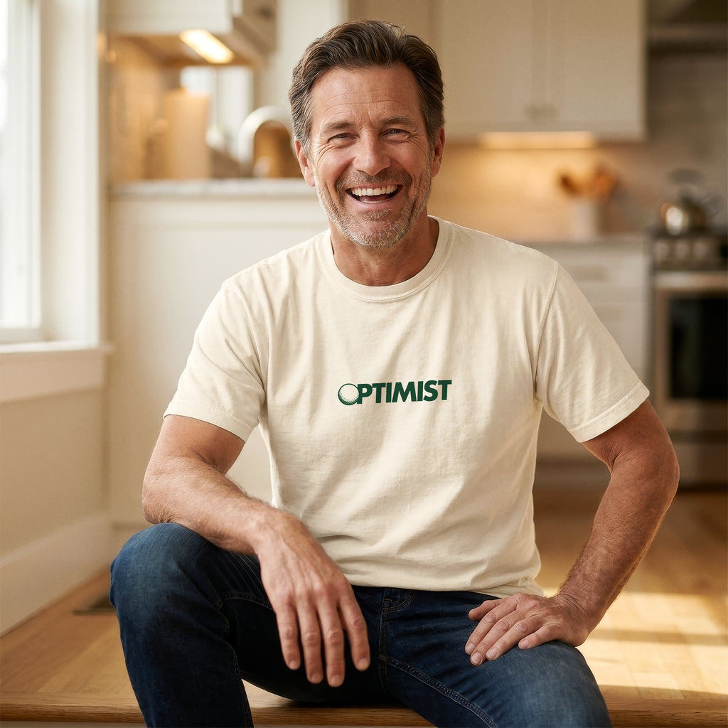 Man wearing an Ivory t-shirt with 'OPTIMIST' printed on it. The "O" in OPTIMIST has been replaced by a golf ball.