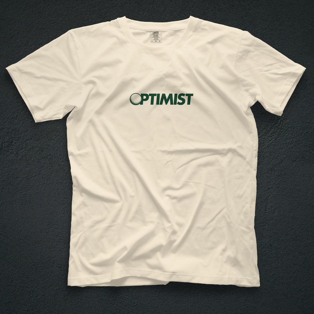 Ivory t-shirt with 'OPTIMIST' printed on it. The "O" in OPTIMIST has been replaced by a golf ball.